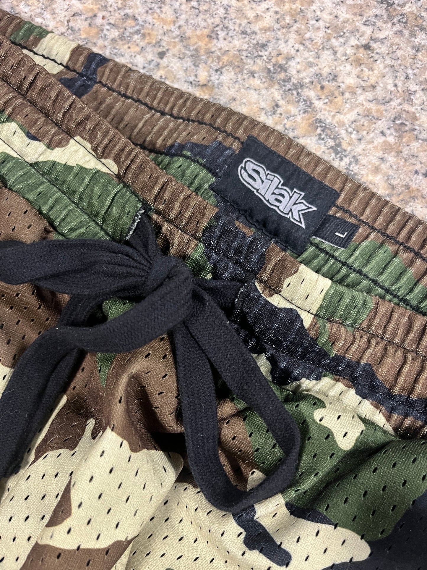 Camouflage-patterned shoe with black laces and a visible brand label on a textured surface.